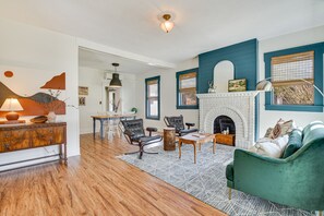 Een woonkamer met een open haard, houten vloeren en een groene bank.