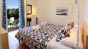 Quarto de hotel com cama, escrivaninha, cadeira, luminária e vista para o exterior.