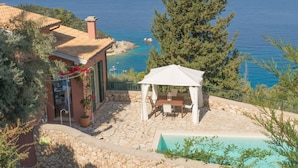 Um pátio de pedra com piscina, um gazebo e vista para o mar.