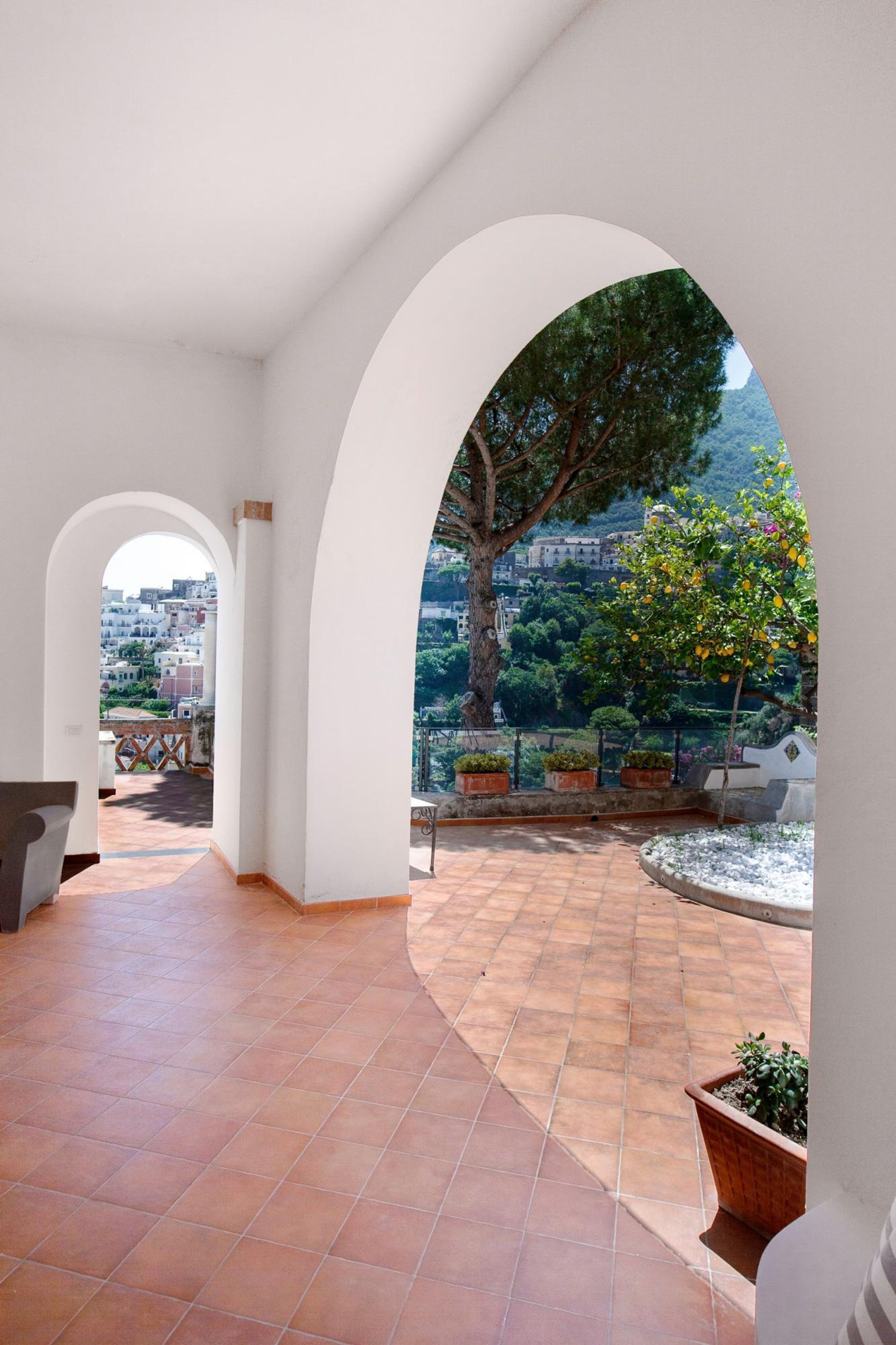An interior courtyard with arches, a tiled floor, and a view of a tree and buildings in the distance.