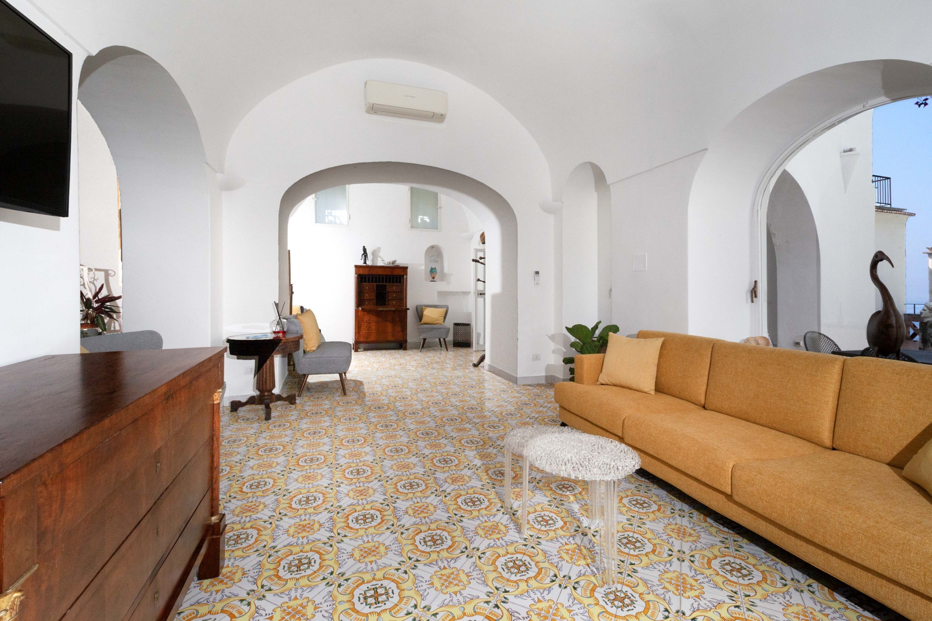A spacious living area with a patterned floor, a sofa, a wooden dresser, and a small table.
