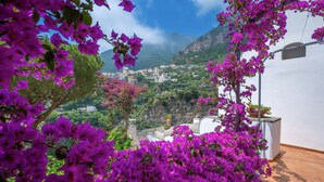 A balcony with purple bougainvillea flowers, a white building, and a mountainous landscape in the background. - Villa Field in Positano (Positano)