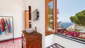 A bathroom with a wooden vanity, a large mirror, and a view of a coastal town through a window. - Villa Field in Positano (Positano)