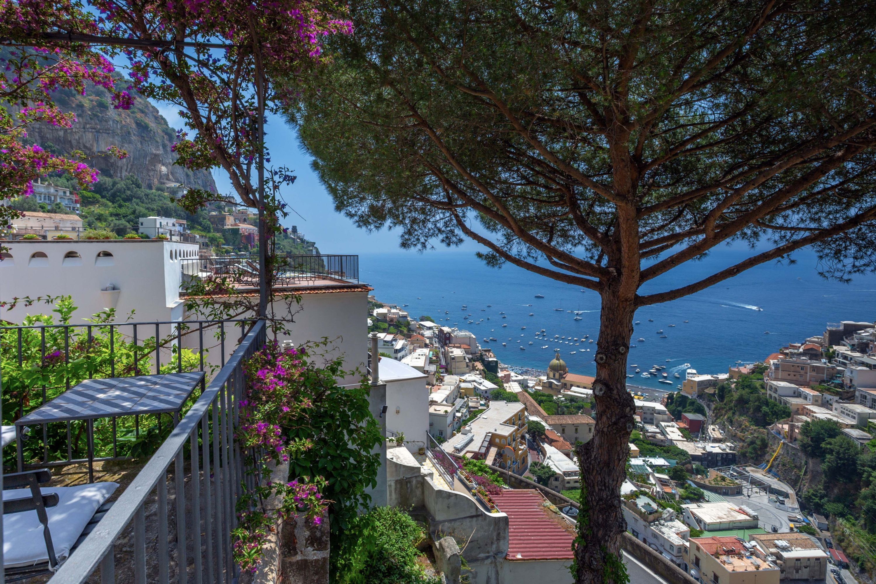 Uma vila costeira com edifícios, uma árvore e vista para o mar.