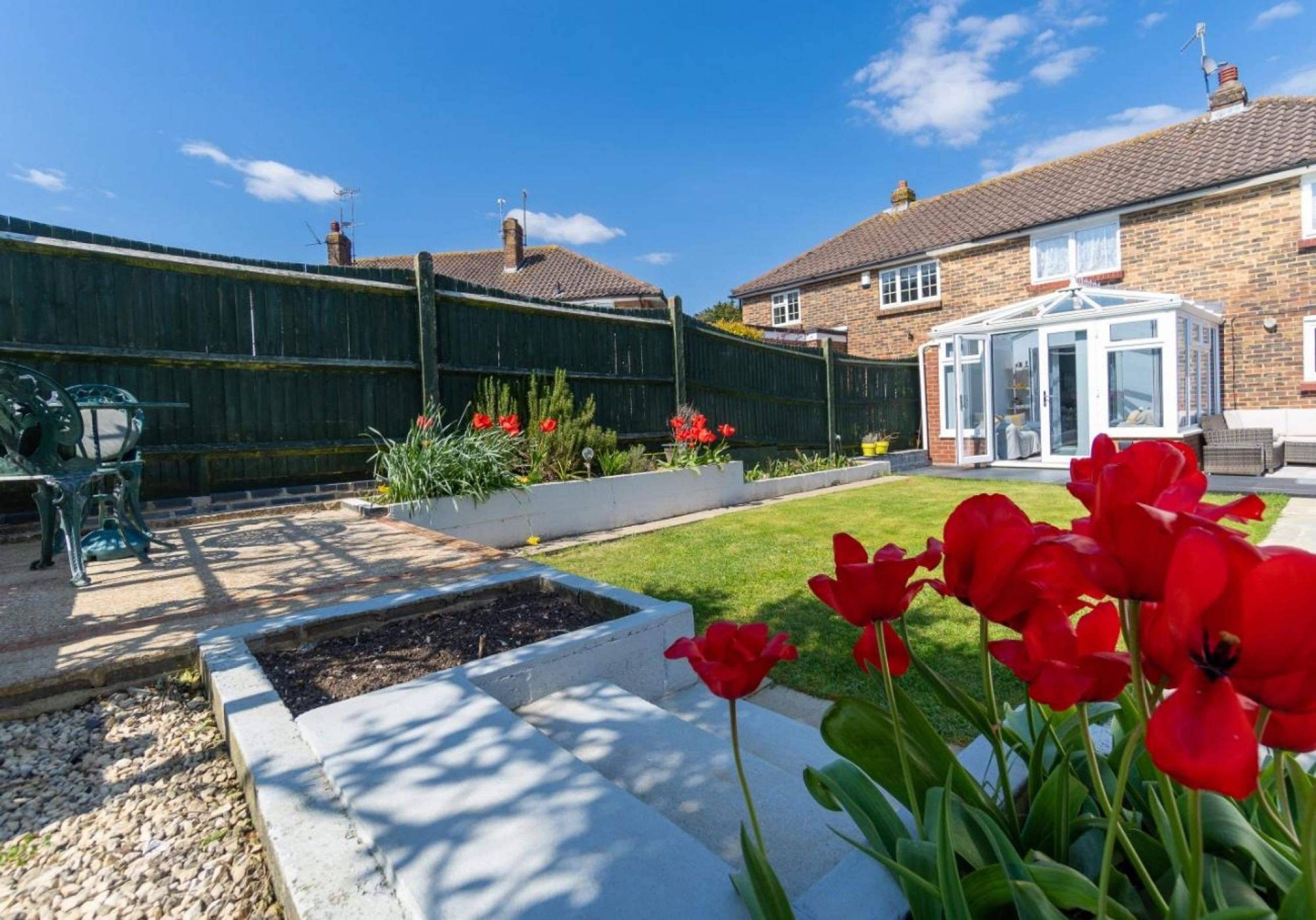 A garden with red tulips, a wooden fence, and a conservatory.