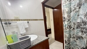 A bathroom with a granite countertop, a sink, a mirror, and a shower curtain with a leaf pattern. - St. Lawrence Suites - Suite Two (Oistins)