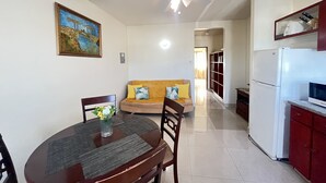 A dining area with a round table, chairs, and a ceiling fan. A sofa with cushions is visible in the background. - St. Lawrence Suites - Suite Two (Oistins)