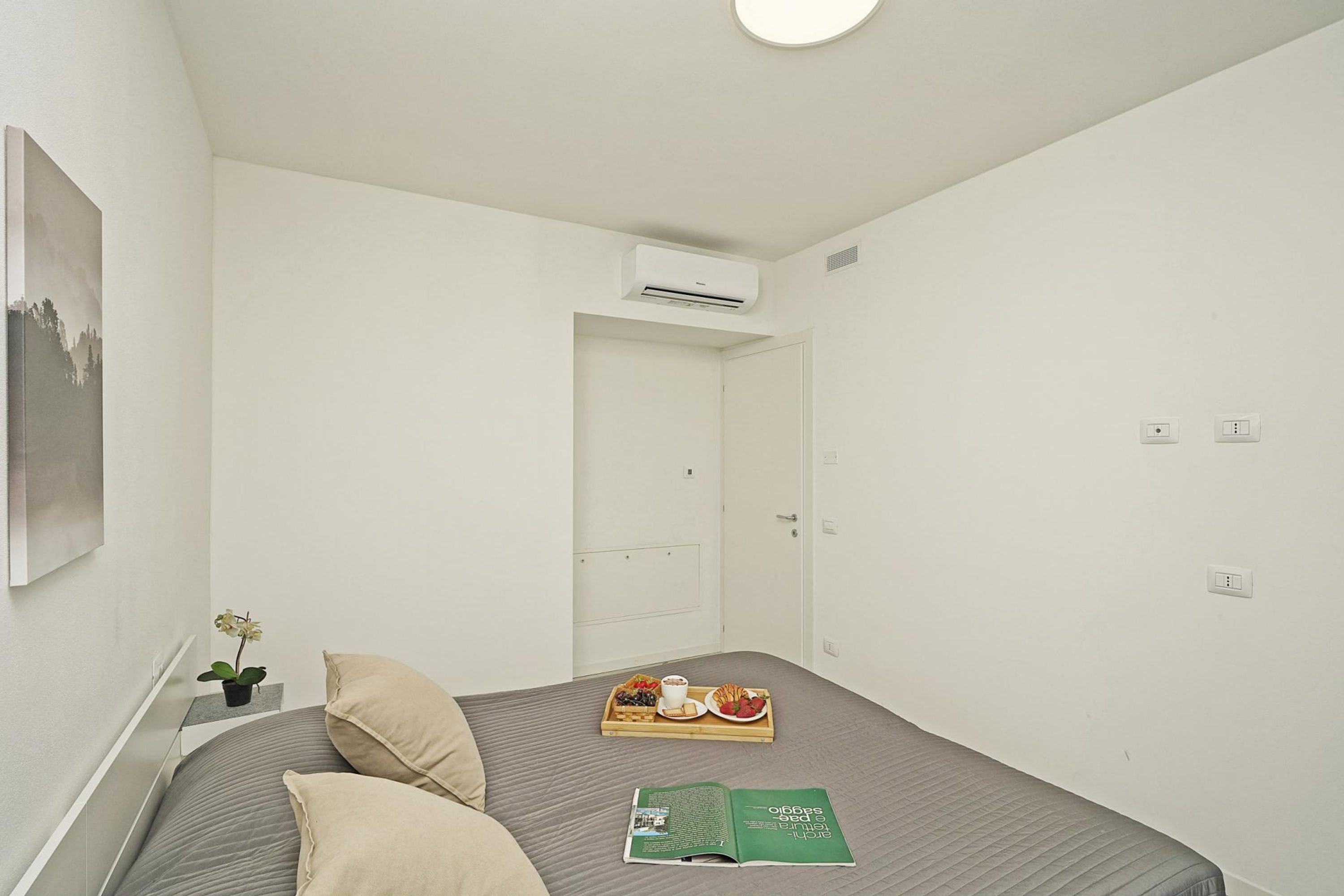 Un dormitorio ordenado con una cama, una bandeja de desayuno, un libro y una planta en maceta.
