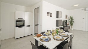 Eine moderne Küche mit weißen Schränken, einem eingebauten Backofen und einem Essbereich mit Tisch für vier Personen.