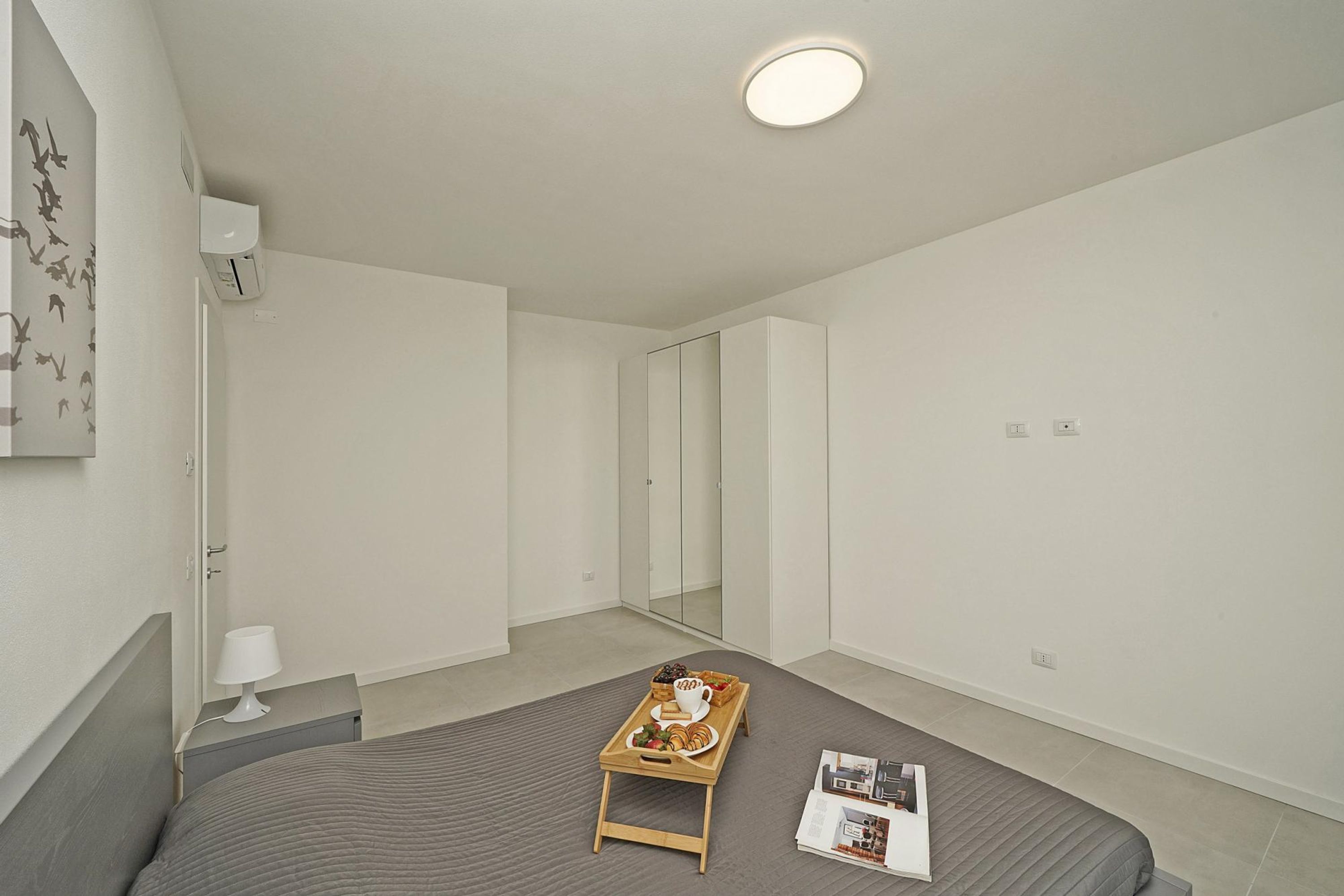A minimalist bedroom with a bed, bedside table, and a tray with breakfast items.