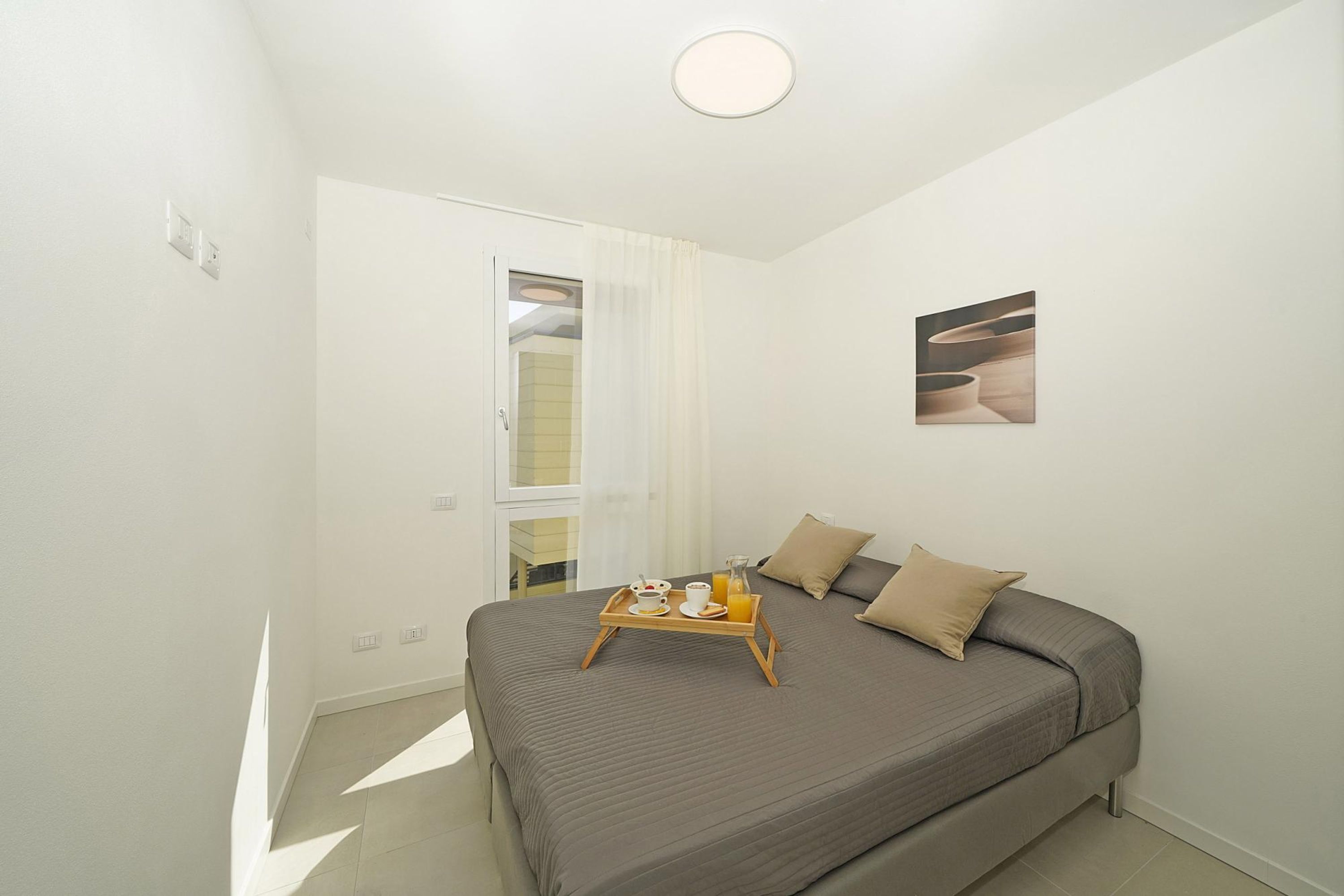 A modern bedroom with a large bed, a breakfast tray, and a painting on the wall.