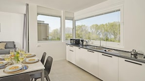 A modern kitchen with white cabinets, a black countertop, and large windows offering a view of trees. - Katya Resort A1 10 by Wonderful Italy (Desenzano del Garda)