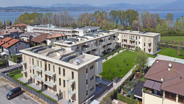 A modern apartment complex with multiple buildings, balconies, and a view of a lake and mountains. - Katya Resort A1 10 by Wonderful Italy (Desenzano del Garda)