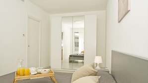 A hotel room with a bed, a bedside table with a lamp, a tray with breakfast items, and a large mirror reflecting the room. - Katya Resort A1 10 by Wonderful Italy (Desenzano del Garda)