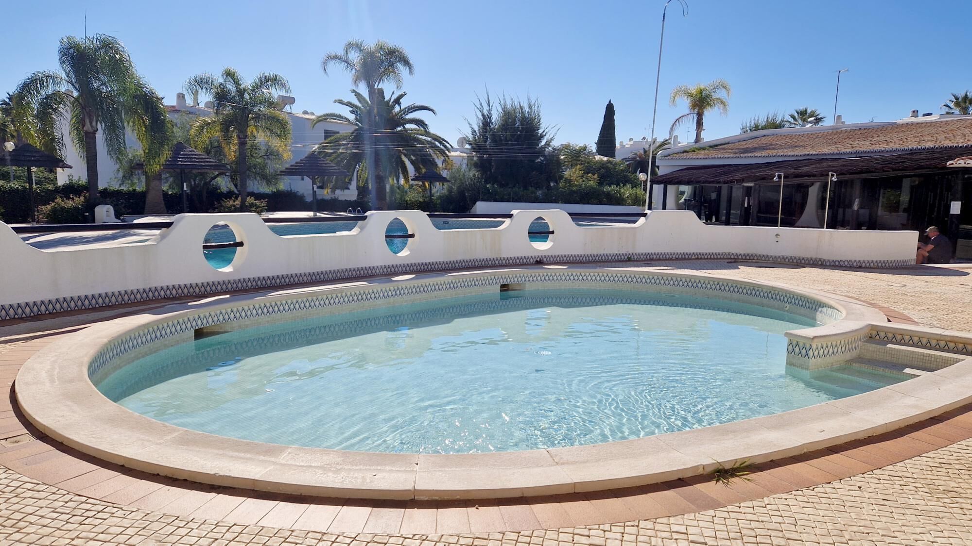 Una piscina con borde alicatado, rodeada por un muro bajo con aberturas circulares.