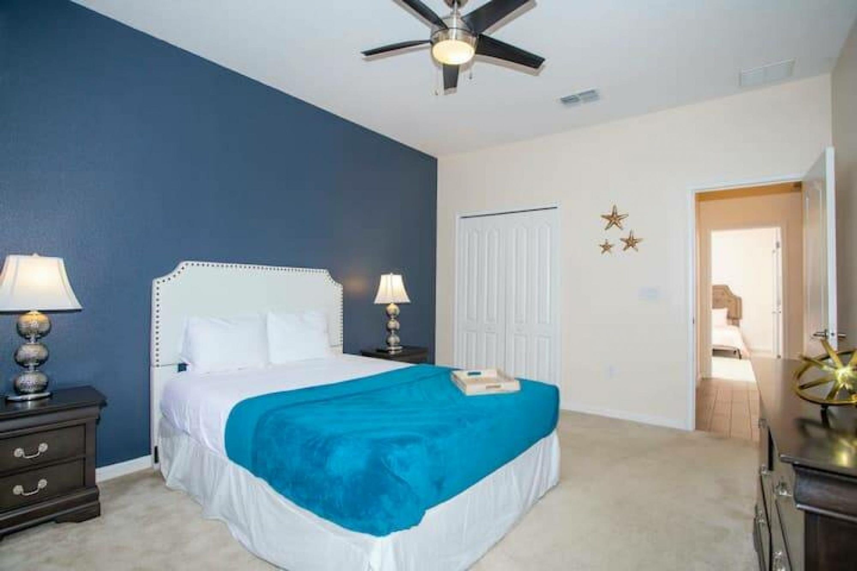 A bedroom with a bed, two bedside tables, a ceiling fan, and a door.