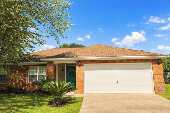 A single-story house with a brick facade, a green front door, a garage, and a small front yard with a palm tree. - 4 Minutes to Navarre Beach, Pet Friendly, Huge Yard (Navarre)