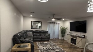 A modern living room with a black leather sofa, a wooden coffee table, a patterned rug, a flat-screen TV, and a fireplace.