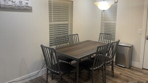 A dining area with a wooden table and four chairs, a small refrigerator, and a ceiling light fixture.