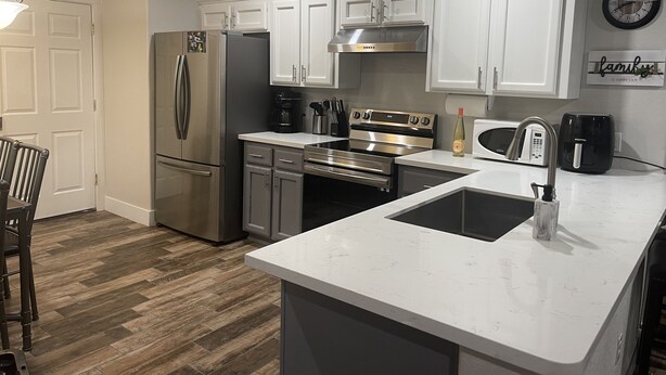 A modern kitchen with white cabinets, stainless steel appliances, and a marble countertop.