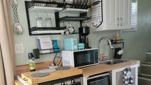 Una kitchenette compacta con microondas, dos hornos, cafetera y escurreplatos.