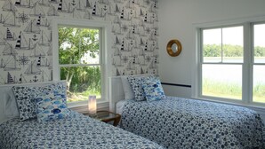 Ein Schlafzimmer mit zwei Betten, maritime Wandgestaltung, einem großen Fenster mit Seeblick und einer runden Wanduhr.