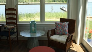 Ein Zimmer mit Seeblick, zwei Korbstühle, ein runder Tisch und ein roter Hocker.