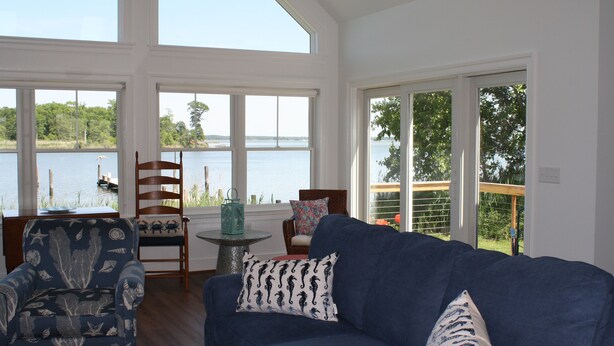 Ein Wohnzimmer mit Seeblick, ein blaues Sofa, gemusterte Kissen und ein Holzstuhl.