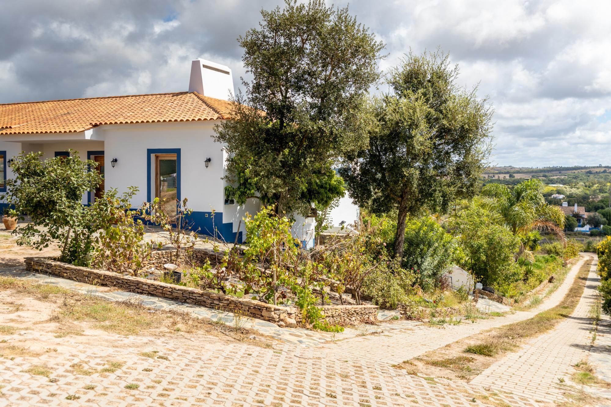 Un bâtiment blanc avec un toit en tuiles et un chemin de pierre menant à l’entrée.