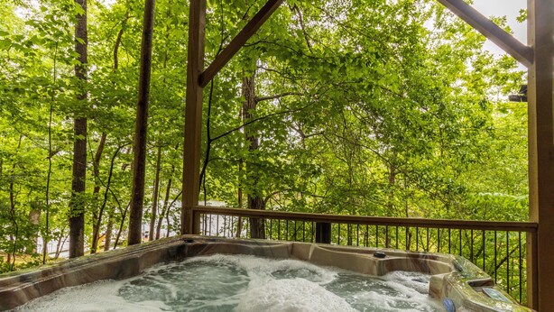 A hot tub surrounded by a wooden deck with a view of a forested area. - Ultimate Entertainment Cabin w/ Theater & Game Room! (Martin)