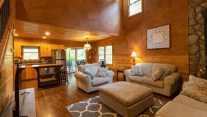 A spacious living area with a kitchen, wooden walls, and a stone accent wall. - Ultimate Entertainment Cabin w/ Theater & Game Room! (Martin)