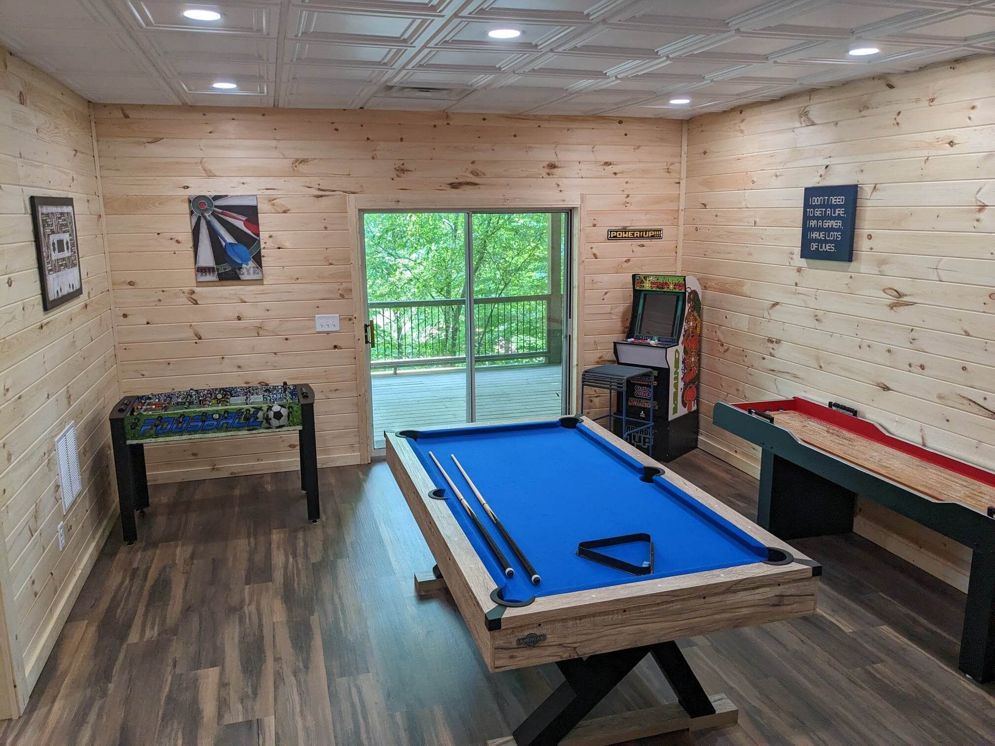 Una mesa de billar en una sala de madera con dardos, una mesa de fútbol de mesa y una máquina de pinball.
