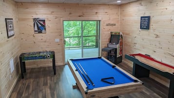 Una mesa de billar en una sala de madera con dardos, una mesa de fútbol de mesa y una máquina de pinball.