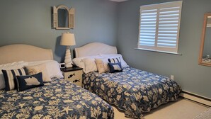 Ein Schlafzimmer mit zwei Betten, einem Deckenventilator, einem Nachttisch mit Lampe, einem Spiegel und einem Fenster mit Jalousien.