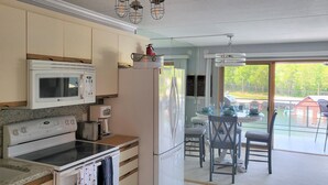 Eine moderne Küche mit Mikrowelle, Herd und Kühlschrank. Es gibt eine Essecke mit Tisch und Stühlen sowie einen Blick ins Freie.