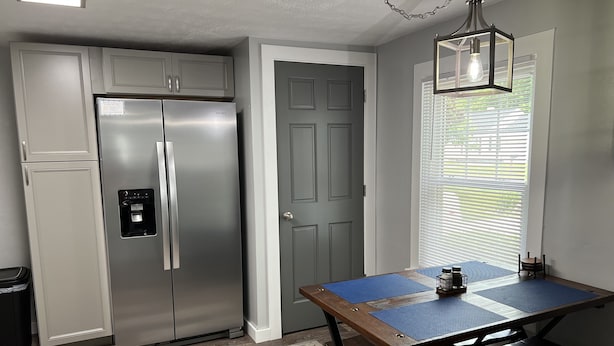 A kitchen with a stainless steel refrigerator, a wooden table with benches, and a window with blinds. - Top-Rated Home Near Ball State & IU Hospital- Top Guest Pick!  (Muncie)