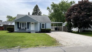 A single-story house with a front porch, a covered entryway, and a driveway leading to a garage. - Top-Rated Home Near Ball State & IU Hospital- Top Guest Pick!  (Muncie)