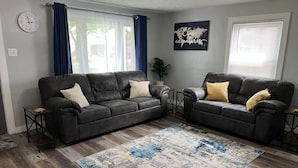 A living room with two dark leather sofas, a patterned rug, a world map artwork, and a clock on the wall. - Top-Rated Home Near Ball State & IU Hospital- Top Guest Pick!  (Muncie)