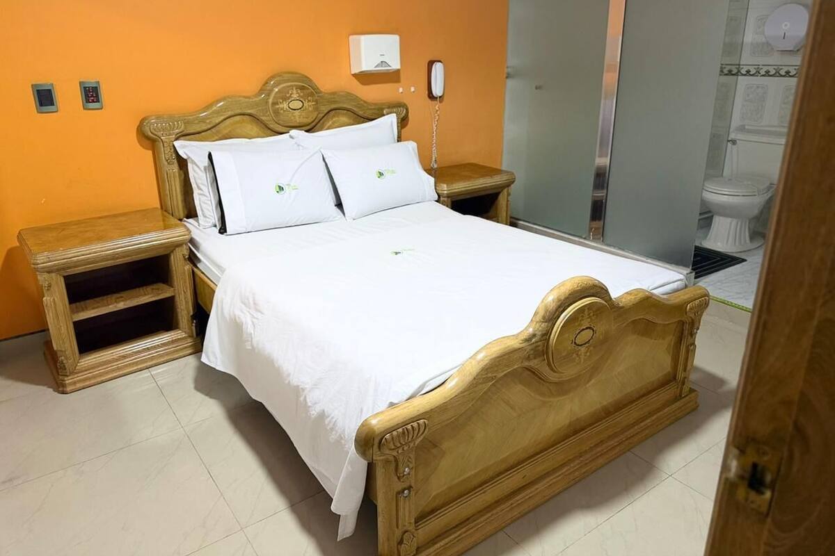 Una cama de madera con ropa de cama blanca en una habitación con paredes naranjas.