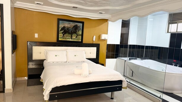A bedroom with a large bed, a mounted TV, a painting of a horse, and a modern bathroom with a bathtub. - Hotel Bosque Chapinero (Bogotá)