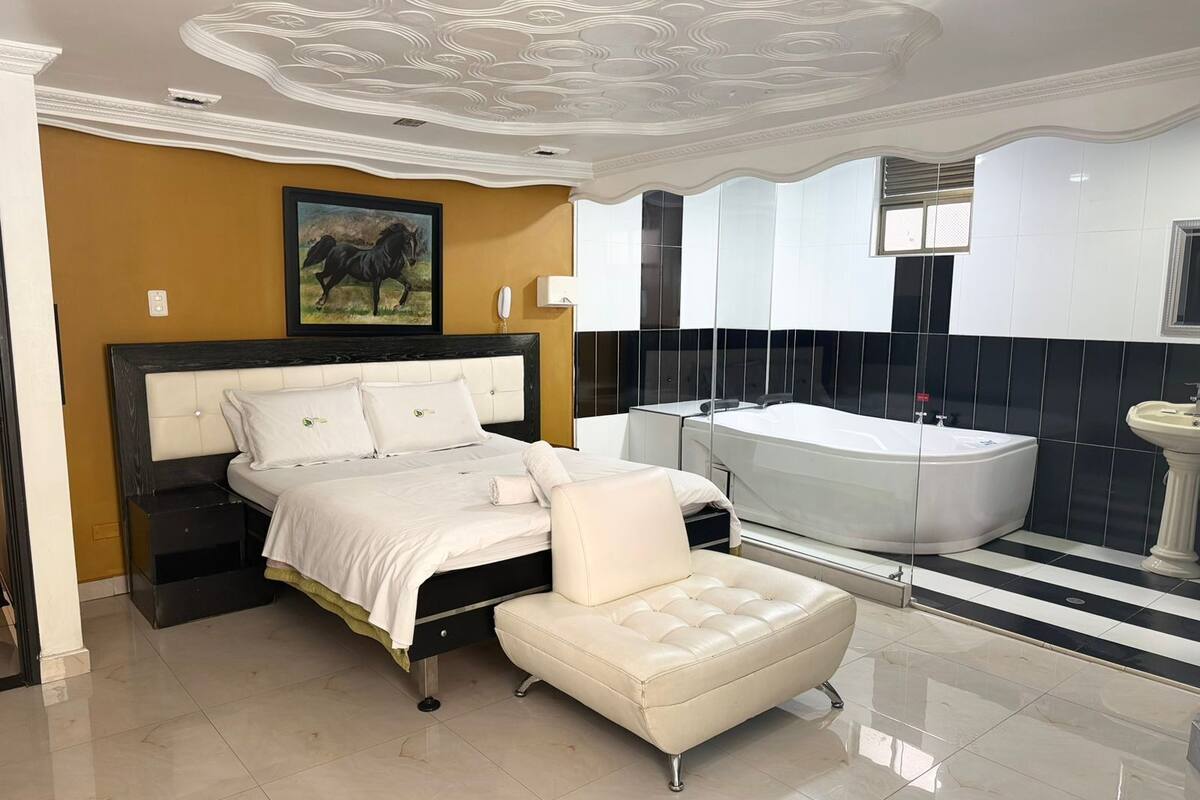 Un dormitorio moderno con una cama grande, una zona de estar, una bañera y un baño con lavabo y espejo.