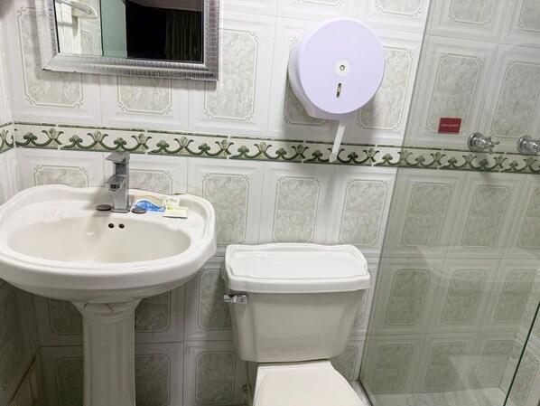 A bathroom with a pedestal sink, toilet, and a paper towel dispenser.
