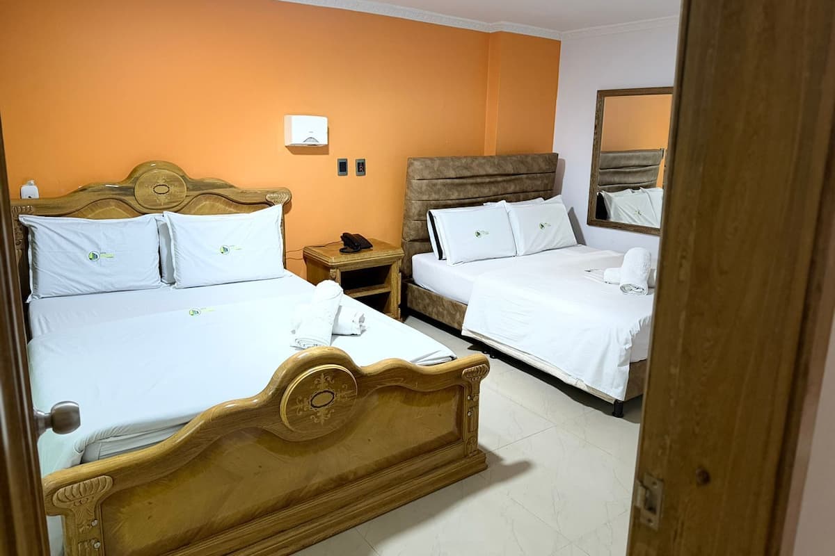 Habitación de hotel con dos camas, cabecero de madera, mesita de noche, espejo y lámpara de pared.