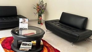 A modern living room with a black leather sofa, a glass coffee table with magazines, and a red and orange rug. - Hotel Bosque Chapinero (Bogotá)