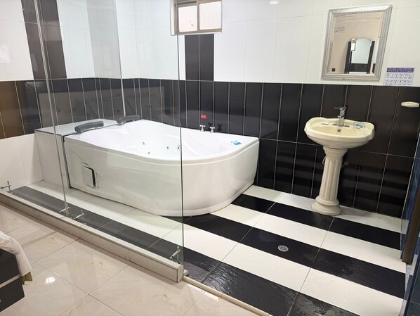 A modern bathroom with a glass-enclosed bathtub, a pedestal sink, and black and white tiled flooring.