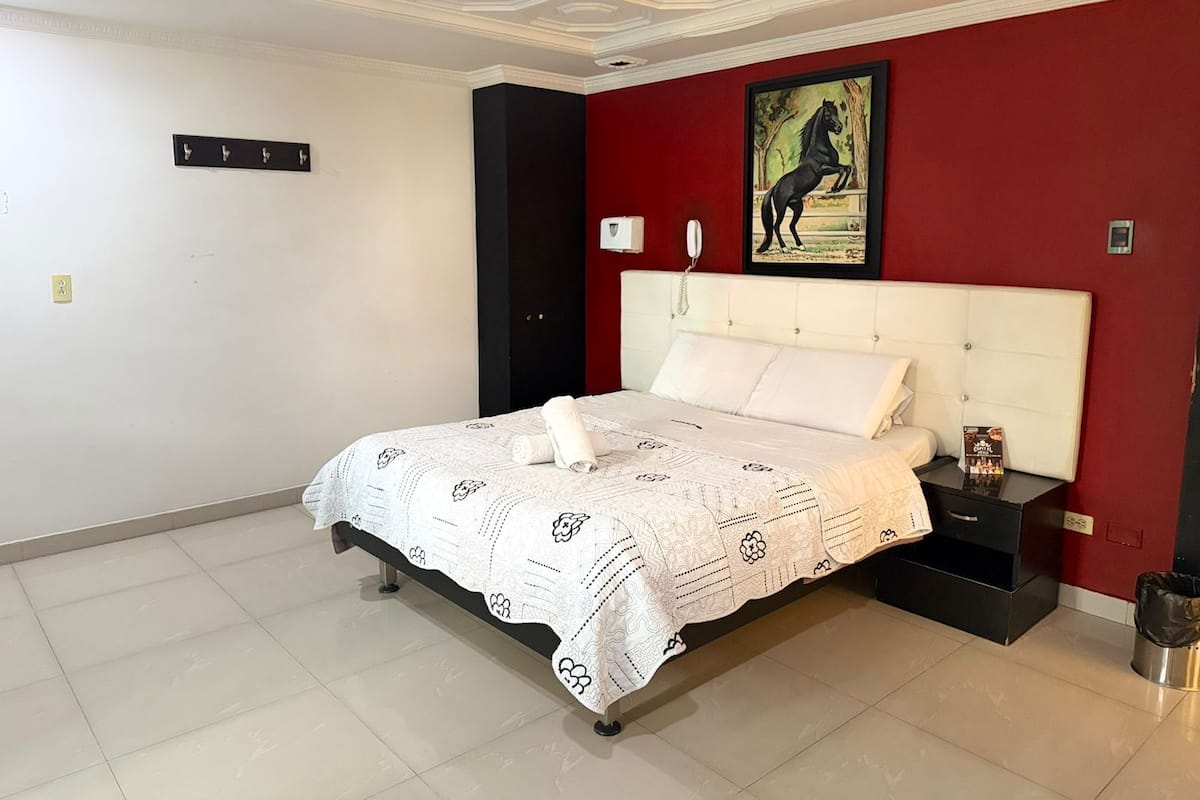 Habitación de hotel con una cama grande, una pared de acento roja, un teléfono montado y un cuadro de un caballo.