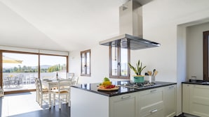 Une cuisine moderne dotée d’un îlot central, de meubles blancs et d’une grande fenêtre donnant sur un paysage magnifique.