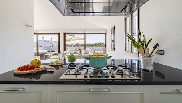 Une cuisine moderne dotée d’un plan de travail noir, d’une hotte en acier inoxydable et offrant une vue sur la terrasse extérieure.