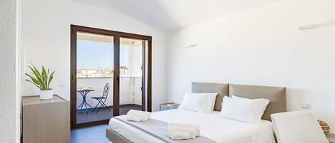 A bedroom with a bed, a bedside table, a chair, a potted plant, and a balcony with a table and chairs.