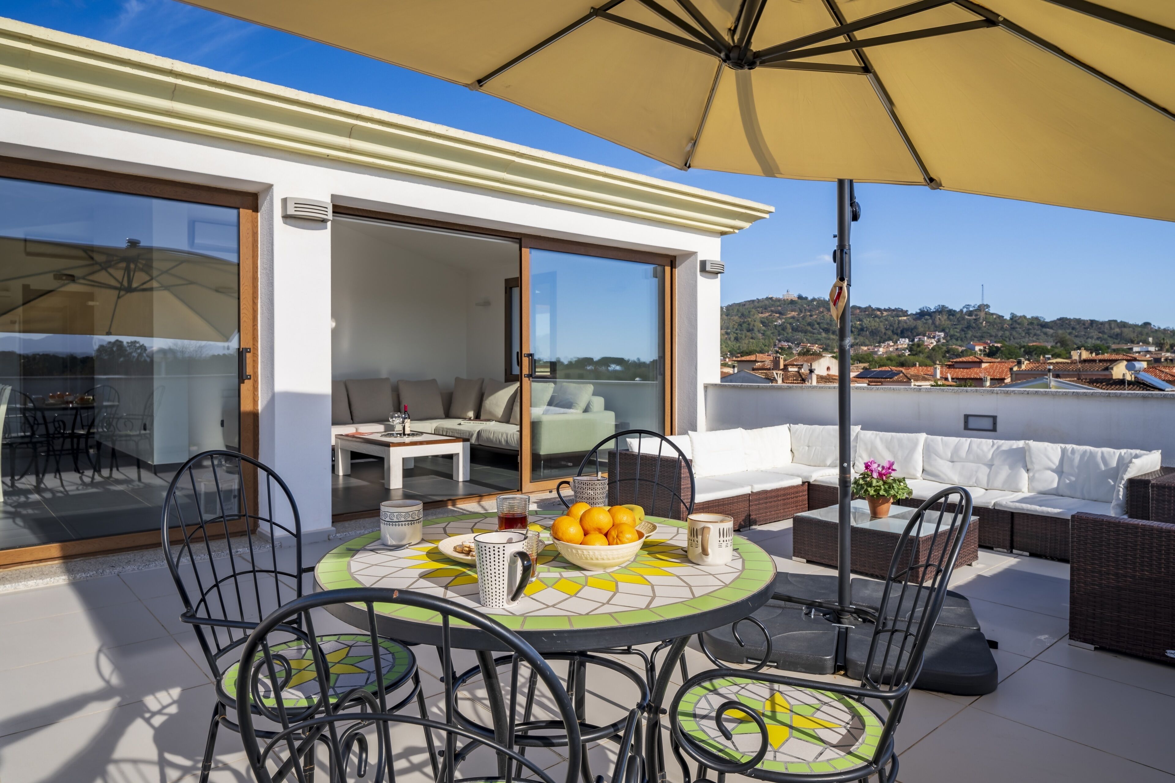 A rooftop terrace with a dining table, chairs, a large umbrella, and a sofa.